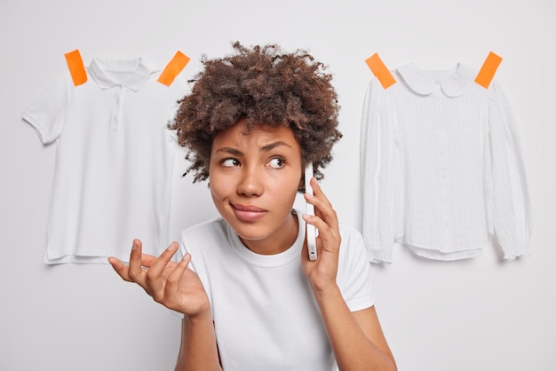 La donna dai capelli piuttosto ricci si sente esitante alza le spalle e fa la telefonata prende una decisione vestita in modo casual posa su uno sfondo bianco con maglietta e camicetta intonacate quindi cosa fare