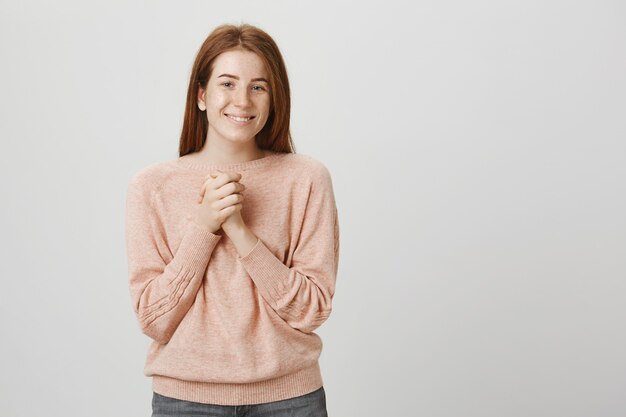 Pretty cute redhead girl clasp hands together, smiling pleased