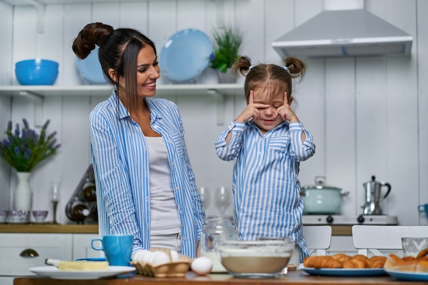 La bella figlia e la sua giovane mamma tirano l'impasto in cucina sul tavolo