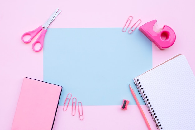  pretty desktop composition with notebook, scissors, and books on pink background with blu