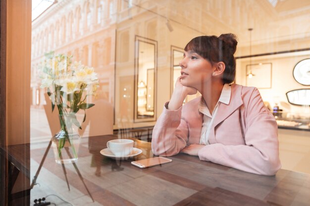 カフェのテーブルに座っているかなり夢を見る若い女性