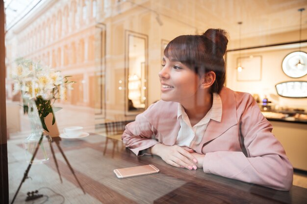 カフェのテーブルに座っているかなり夢を見る若い女性