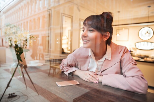 カフェのテーブルに座っているかなり夢を見る若い女性