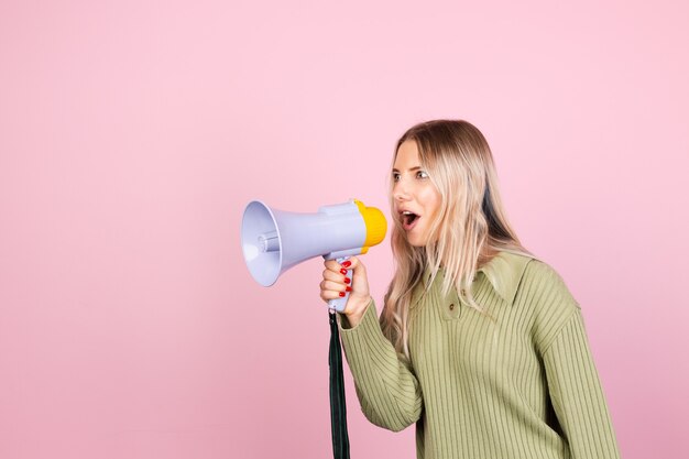 Pretty european woman in casual sweater with megaphone on pink wall