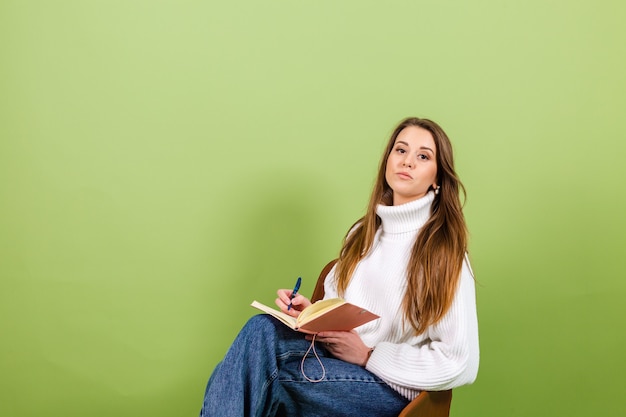 Pretty european woman in casual white sweater isolated, cute happy sit on chair with notepad and pen