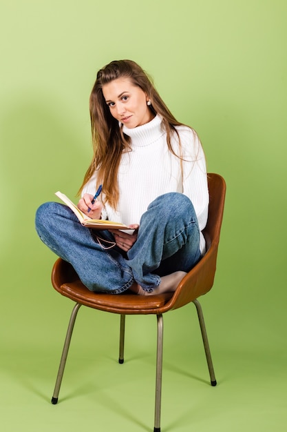 Pretty european woman in casual white sweater isolated, cute happy sit on chair with notepad and pen