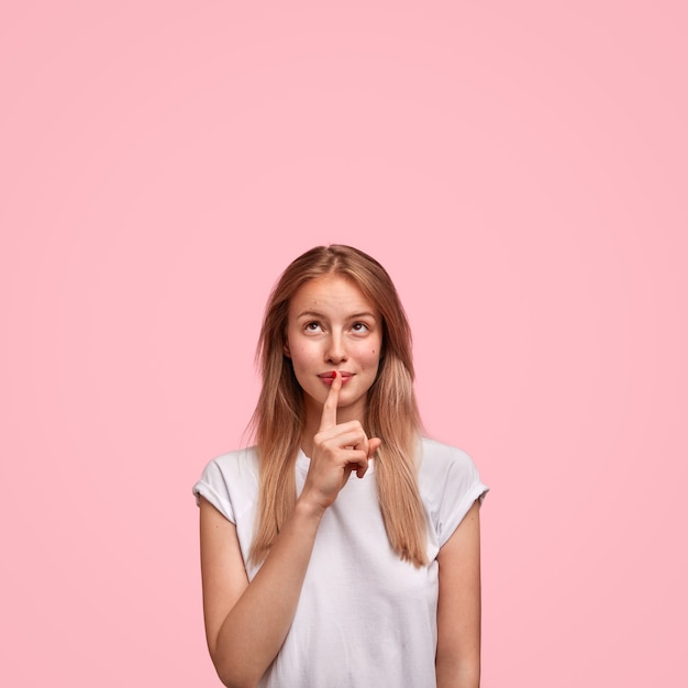 Pretty European young female shows silence sign and asks to keep private information confidential