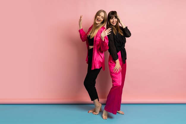 Pretty fashionable women wearing stylish colorful outfit, posing on pink wall