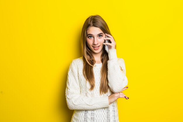 Довольно модная девушка разговаривает по телефону в широком белом свитере на желтом