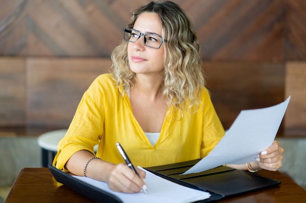 Pretty female business executive working with documents at table