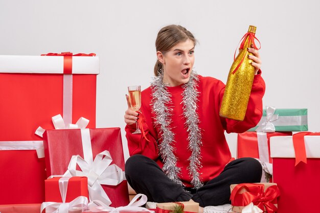 Free photo pretty female sitting around christmas presents celebrating with champagne on white