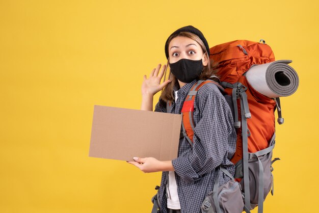 pretty female traveller with black mask and backpack holding cardboard