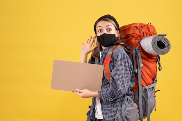 pretty female traveller with black mask and backpack holding cardboard