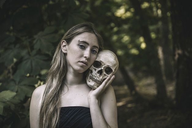 Pretty female with human skull in thicket daytime