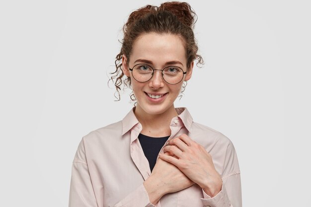 Pretty freckled teenager with glasses posing against the white wall