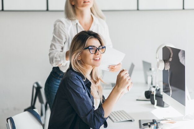 黒い画面でコンピューターの近くに座って、笑顔で目をそらしているかなりフリーランサーの女の子