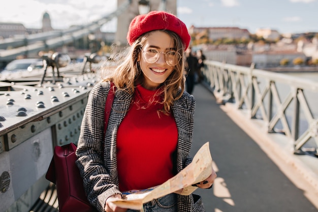 Donna abbastanza francese con mappa della città camminando lungo il ponte in una giornata di sole