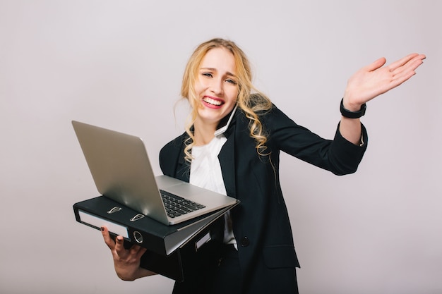 Бесплатное фото Довольно смешная блондинка бизнесмен в костюме с ноутбуком, папкой, коробкой в руках, разговаривает по телефону. стильный офисный работник, занят, развлекается