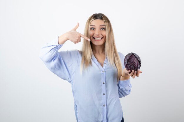 Pretty girl in blue outfit posing with single cabbage on white. 