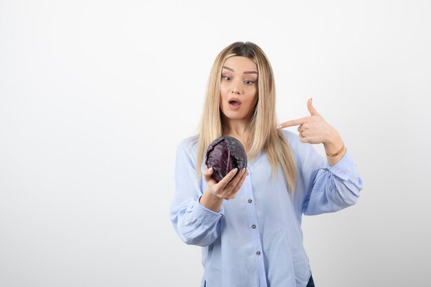 Pretty girl in blue outfit posing with single cabbage on white. 