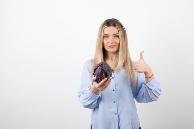 Pretty girl in blue outfit posing with single cabbage on white. 