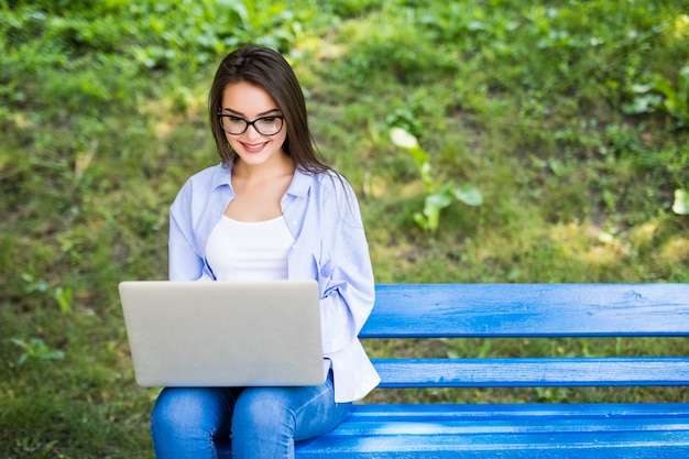 Pretty Girl in blue t-shirt sit on the bench in the park and use her laptop