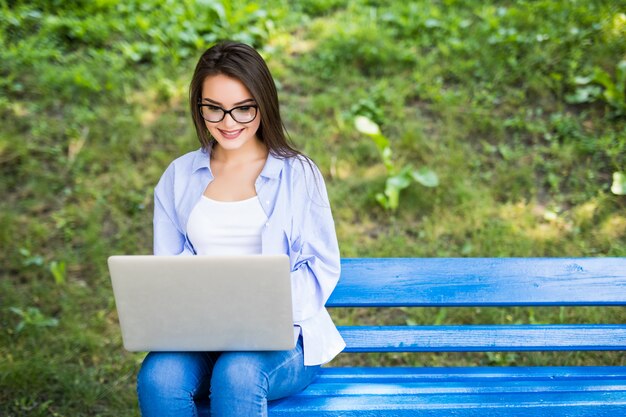 Pretty Girl in blue t-shirt sit on the bench in the park and use her laptop