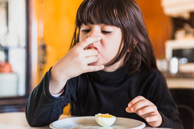 Pretty girl eating half of egg in kitchen