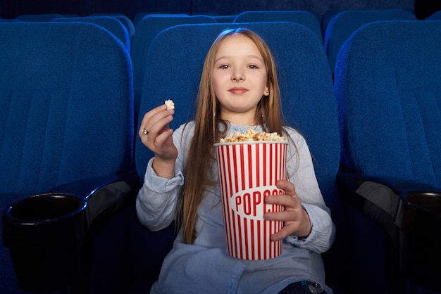 Pretty girl eating popcorn, watching film in cinema.