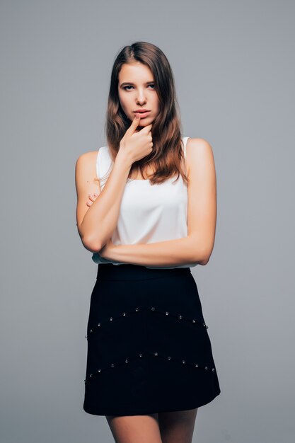 Pretty girl in fashion modern dress is posing in studio holds arm on her chin isolated on white background