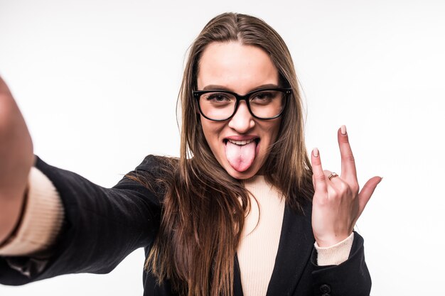 Pretty girl in glasses shows rock sign and tongue out isolated on white