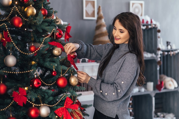 빨간 스웨터와 크리스마스 트리 전에 회색 스웨터 포즈에 예쁜 여자