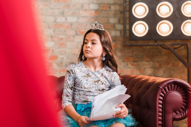 Pretty girl holding scripts sitting on sofa looking away