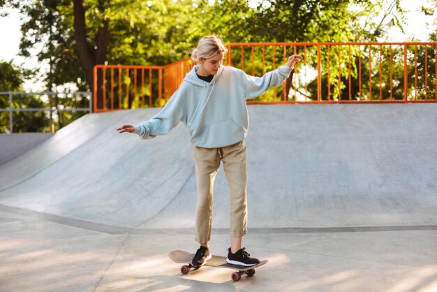 Pretty girl in hoodie trying skateboarding while spending time at modern skatepark