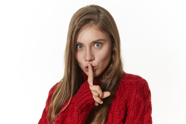 Free Photo pretty girl in knitted sweater holding fore finger at her lips and looking with playful mysterious facial expression, saying shh, let's keep it secret. gestures, signs and body language