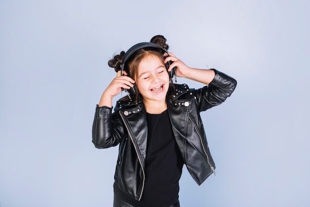 Free photo pretty girl listening music on headphone standing against blue backdrop