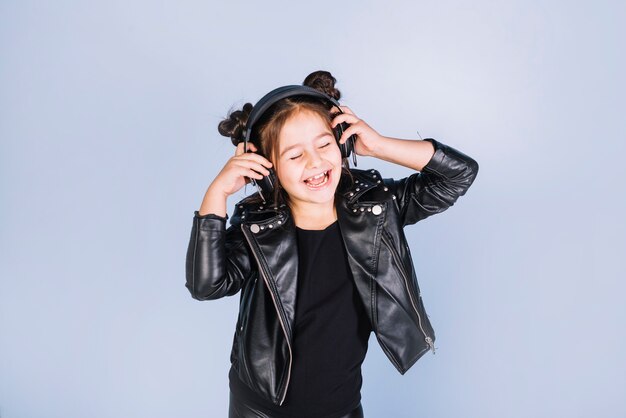 Pretty girl listening music on headphone standing against blue backdrop