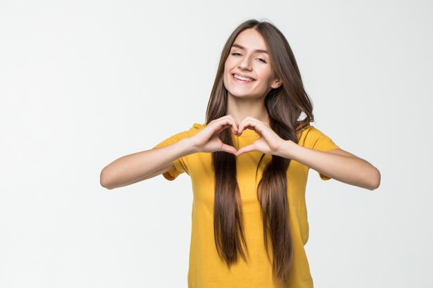 Pretty girl making a heart symbol with her hands over her heart isolated on white wall