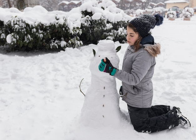 Pretty girl making snowman during winter season