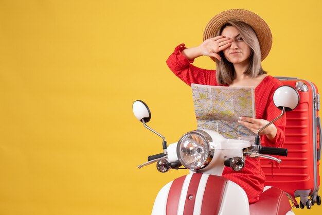 pretty girl on moped with red suitcase holding map covering one eye with hand