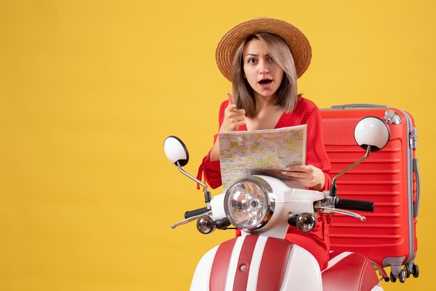 pretty girl on moped with red suitcase holding map pointing at camera