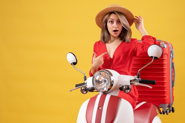 Pretty girl on moped with red suitcase pointing at herself