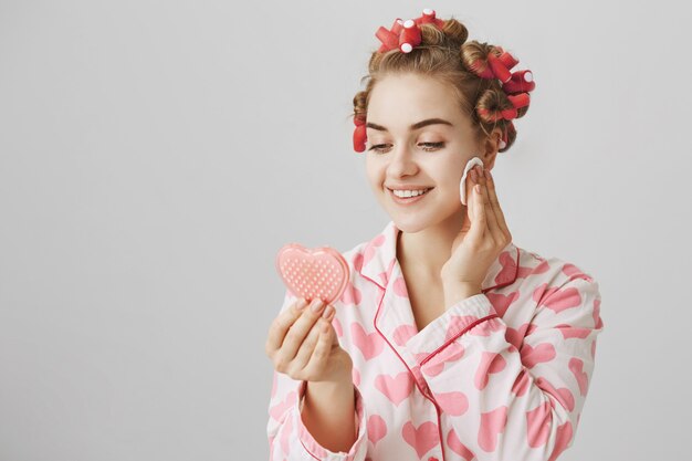 Pretty girl in nighwear and hair curlers, looking mirror and wipe-off makeup up cotton pad