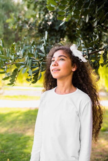 Pretty girl playing with her curly hairs standing in front of tree