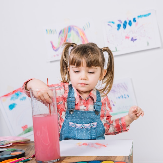 Pretty girl putting paint brush into water glass