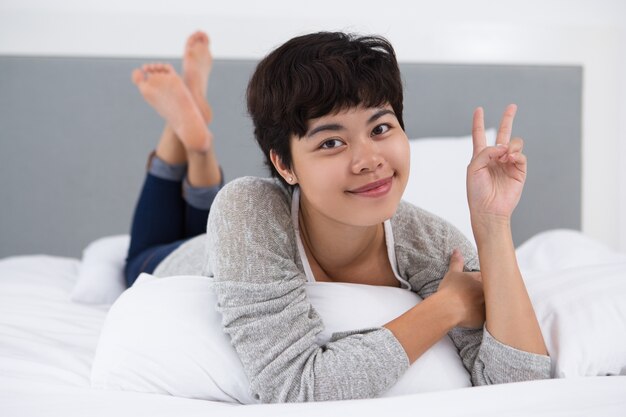 Pretty Girl Resting in Bed Showing Victory Sign