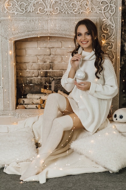 Free photo pretty girl sits near fireplace and holds a christmas toy