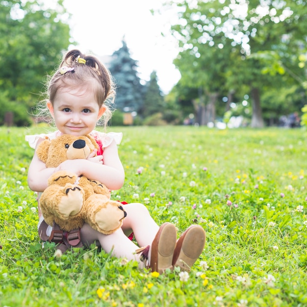 Free photo pretty girl sitting on green grass cuddling her teddy bear