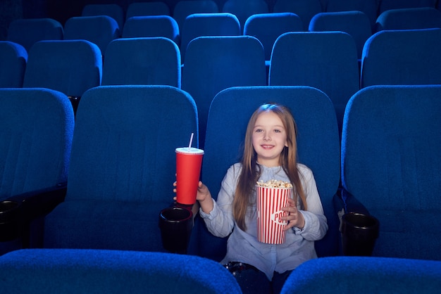 Милая девушка сидя с ведром попкорна в кино.