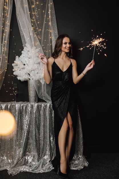 Free photo pretty girl stands near a decoration in silver color and looks at a sparkler